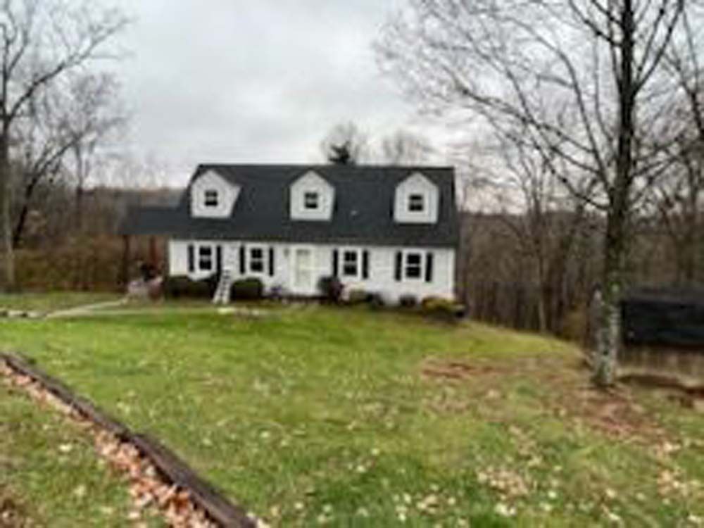 A large white house with a black roof is sitting on top of a hill surrounded by trees.
