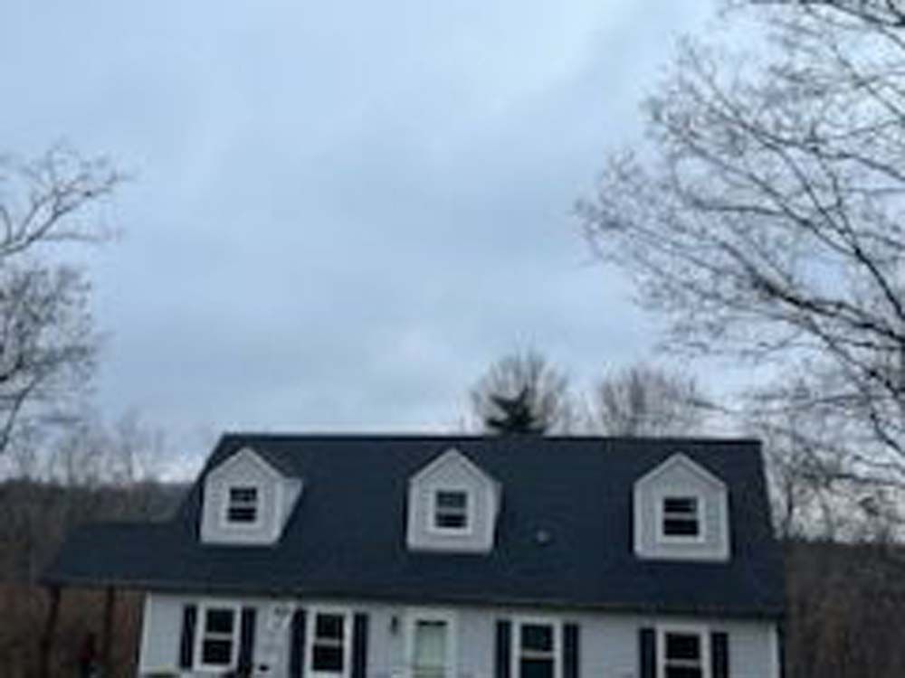 A white house with a black roof is surrounded by trees on a cloudy day.