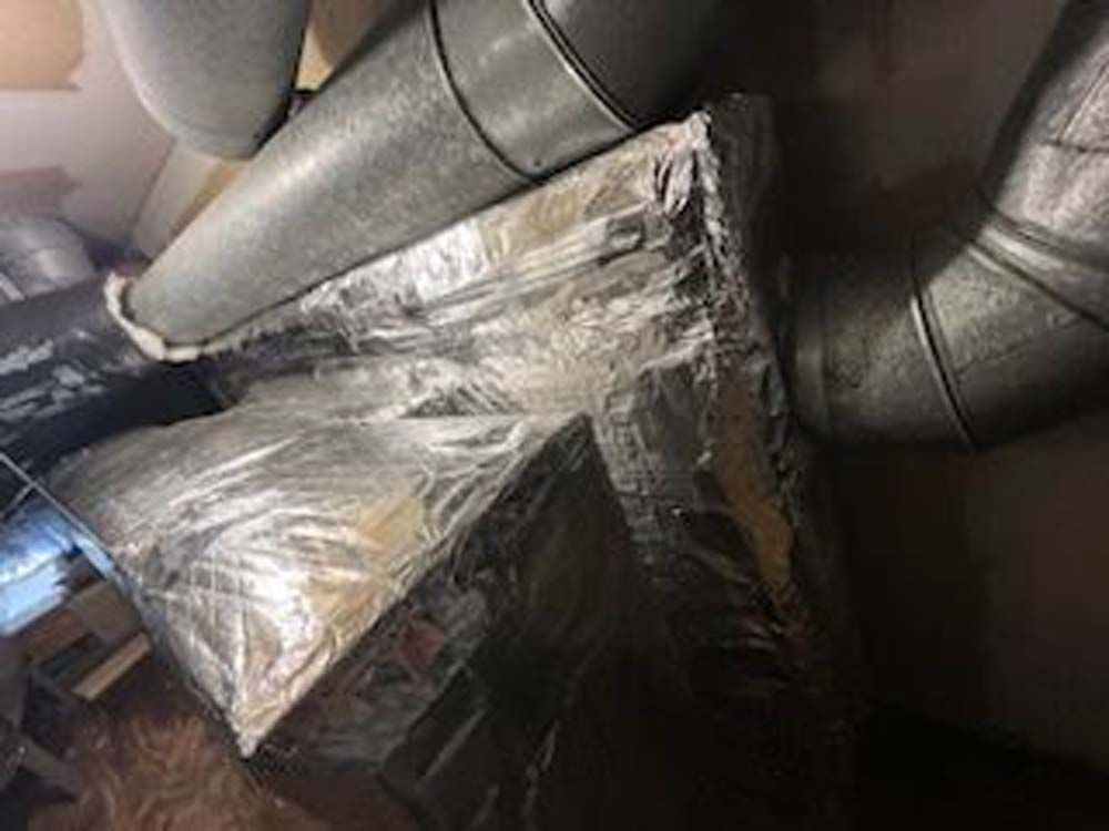 A bunch of pipes are wrapped in plastic and sitting on top of each other in a room.