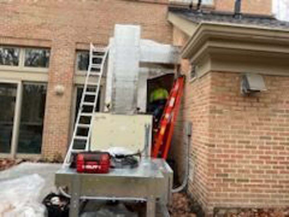A man is standing on a ladder next to a machine in front of a brick building.
