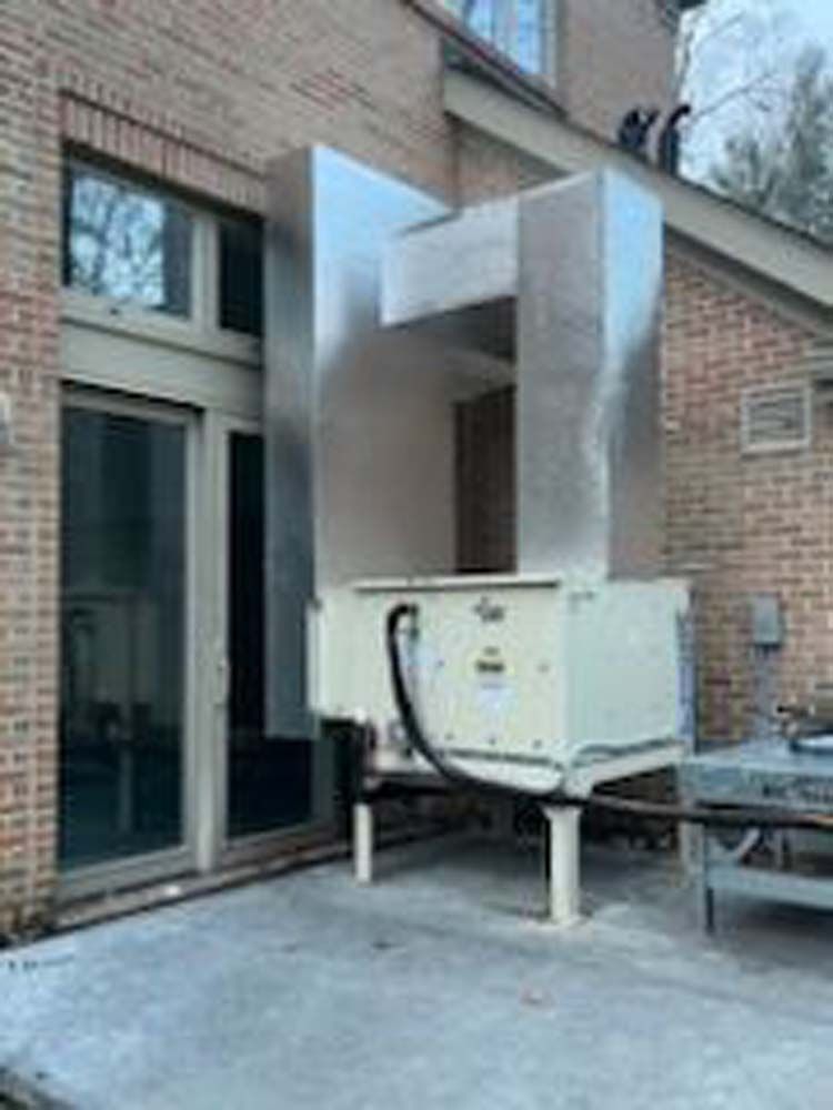 A large machine is sitting outside of a brick building.