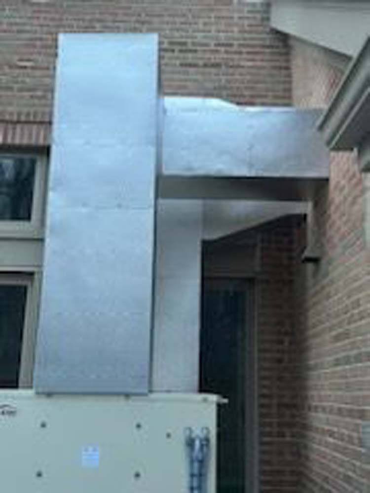 A large metal duct is attached to the side of a brick building.