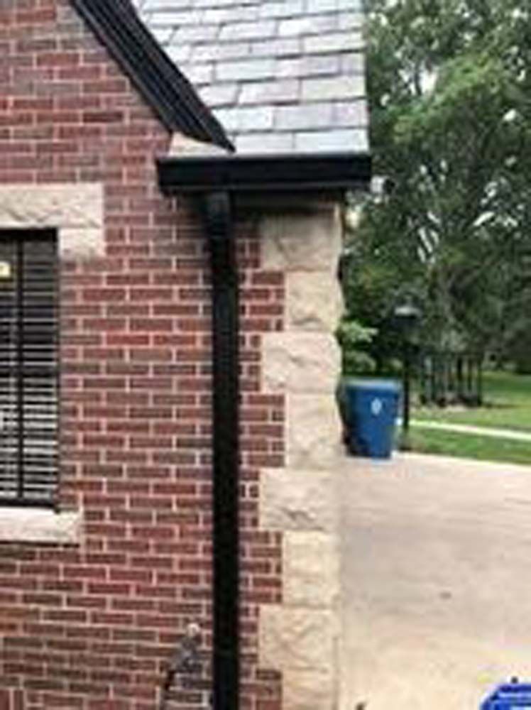 A brick house with a black gutter on the side of it.