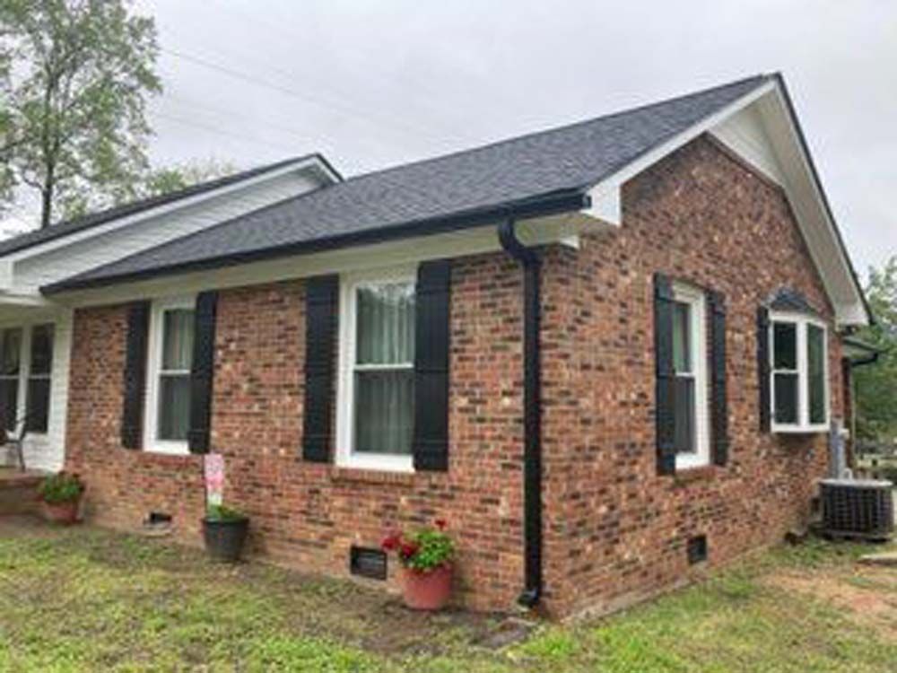 A brick house with black shutters on the windows and a black roof.