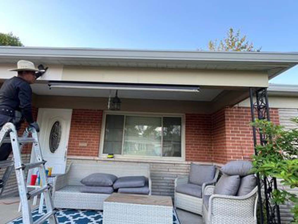 A man is standing on a ladder in front of a brick house.
