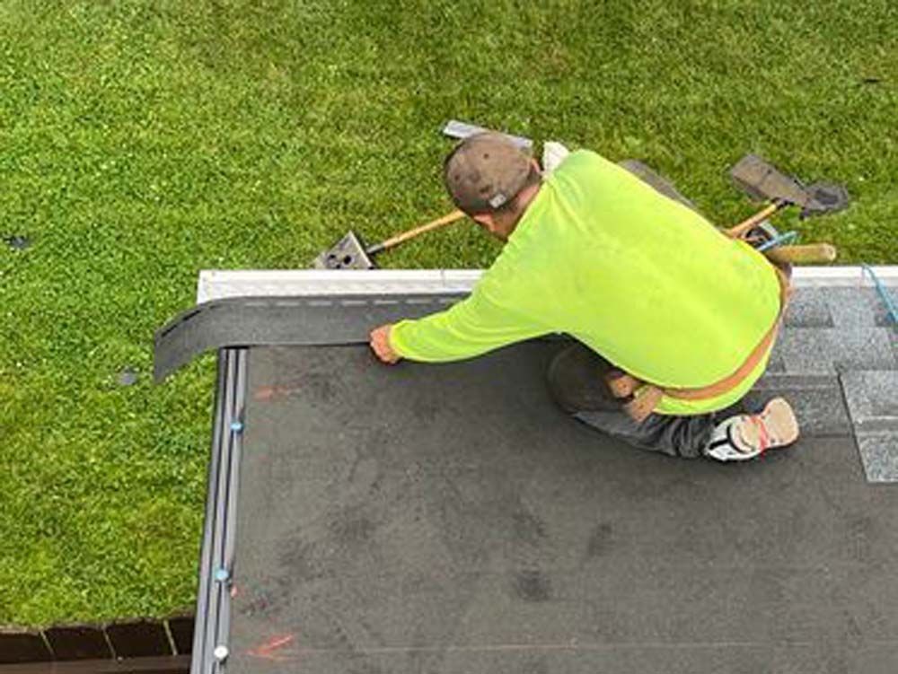 A man is kneeling on the roof of a house.
