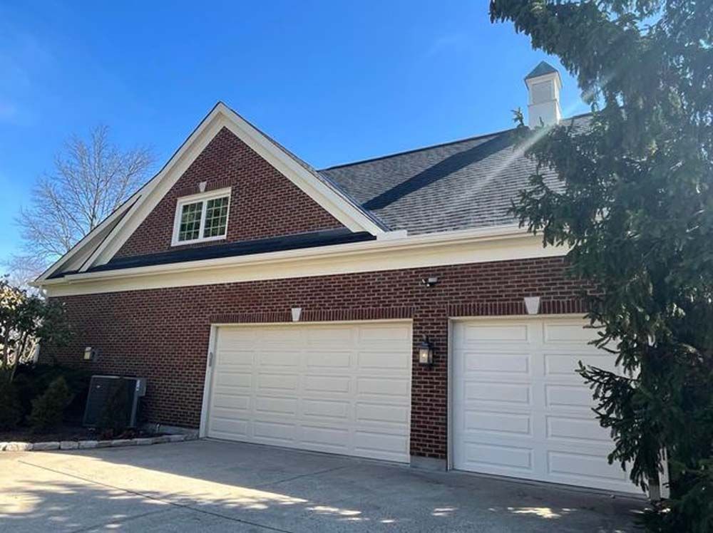 A brick house with two white garage doors and a tree in front of it.