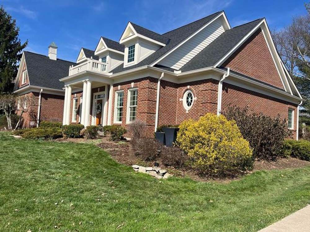 A large brick house with a black roof is sitting on top of a lush green lawn.