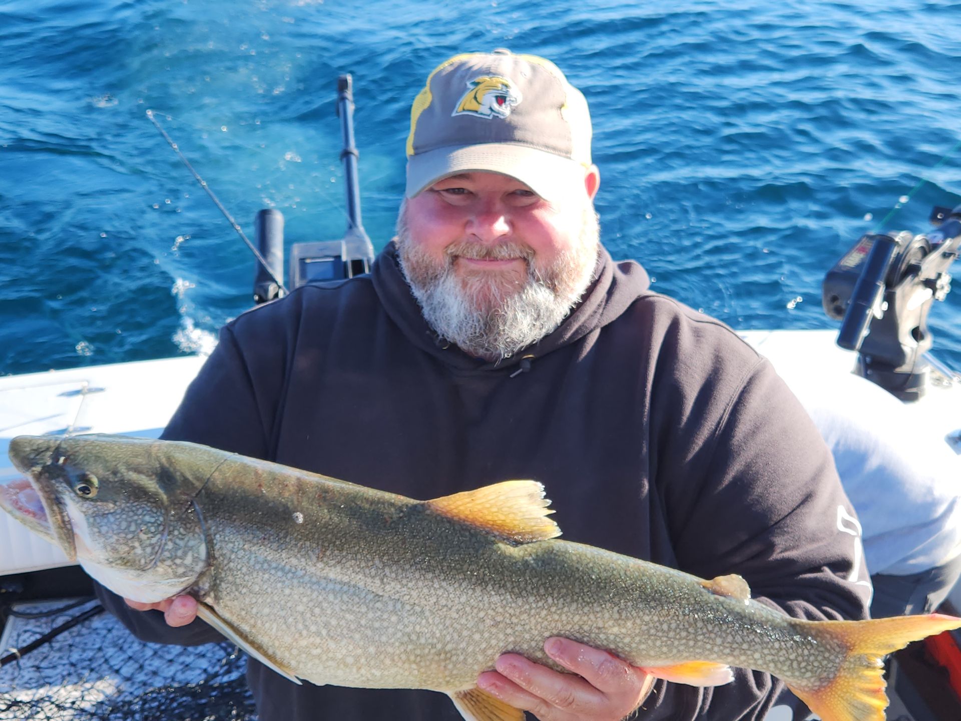 Man in a ball cap holding a large, light-colored fish with orange fins on a boat.