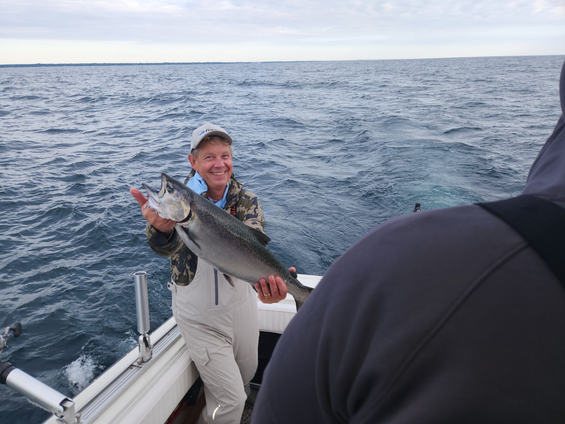 Man on a boat smiles, holding a large fish over water.