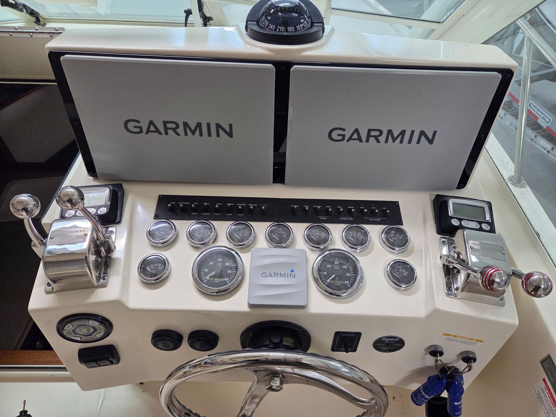 Boat's helm with Garmin displays, gauges, compass, steering wheel, and control levers.
