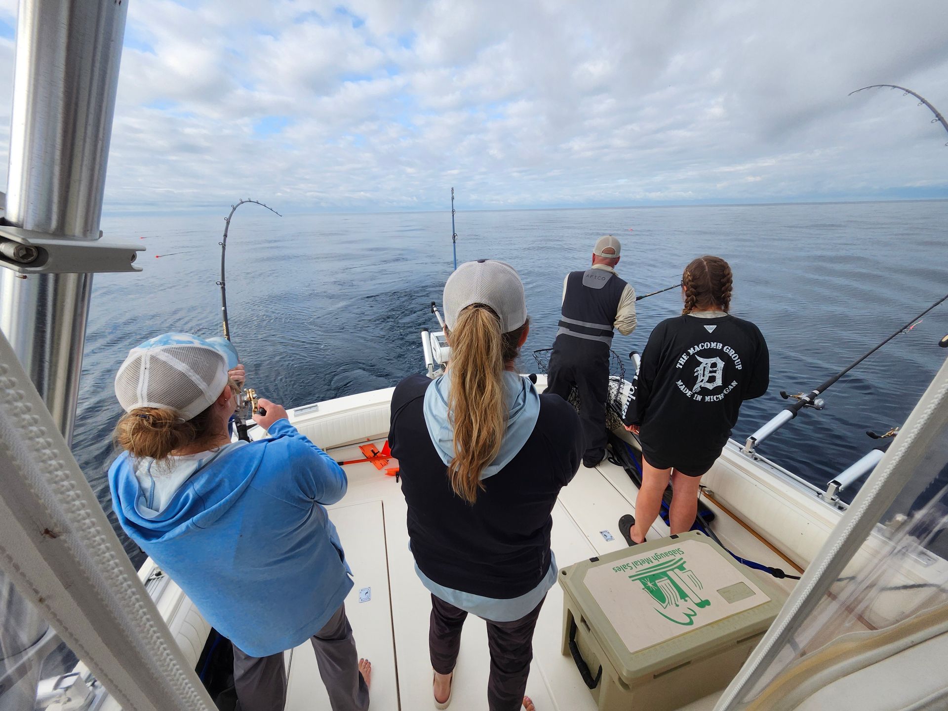 People fishing on a boat in the ocean, rods bent. Cloudy sky, cool tones.