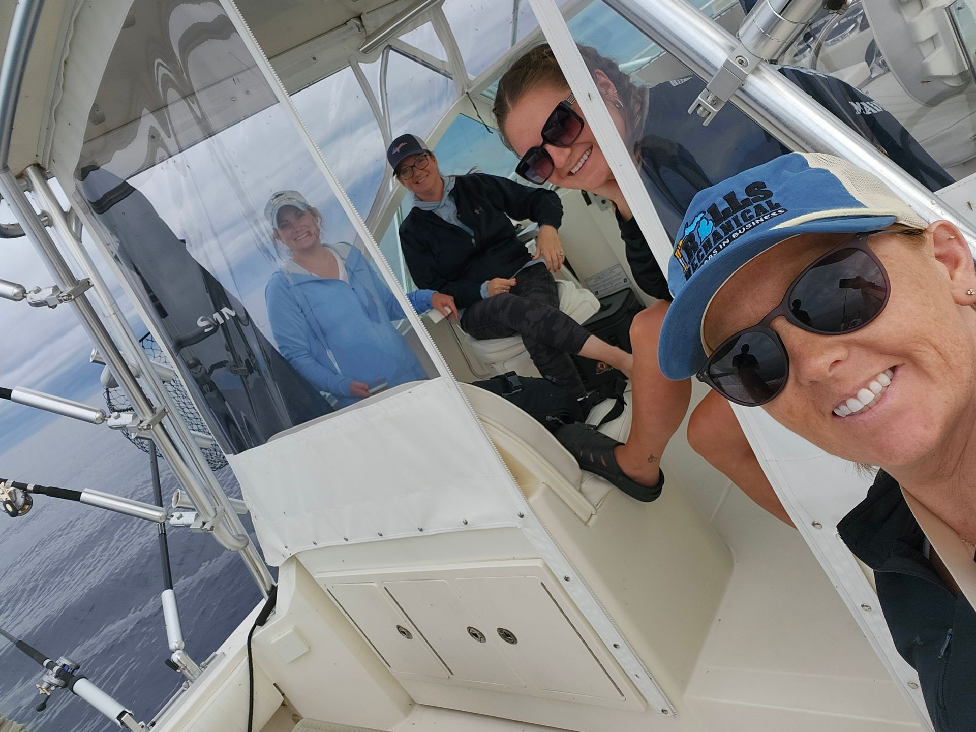 Four people on a boat; one smiling and taking a selfie, others visible through the boat's window.