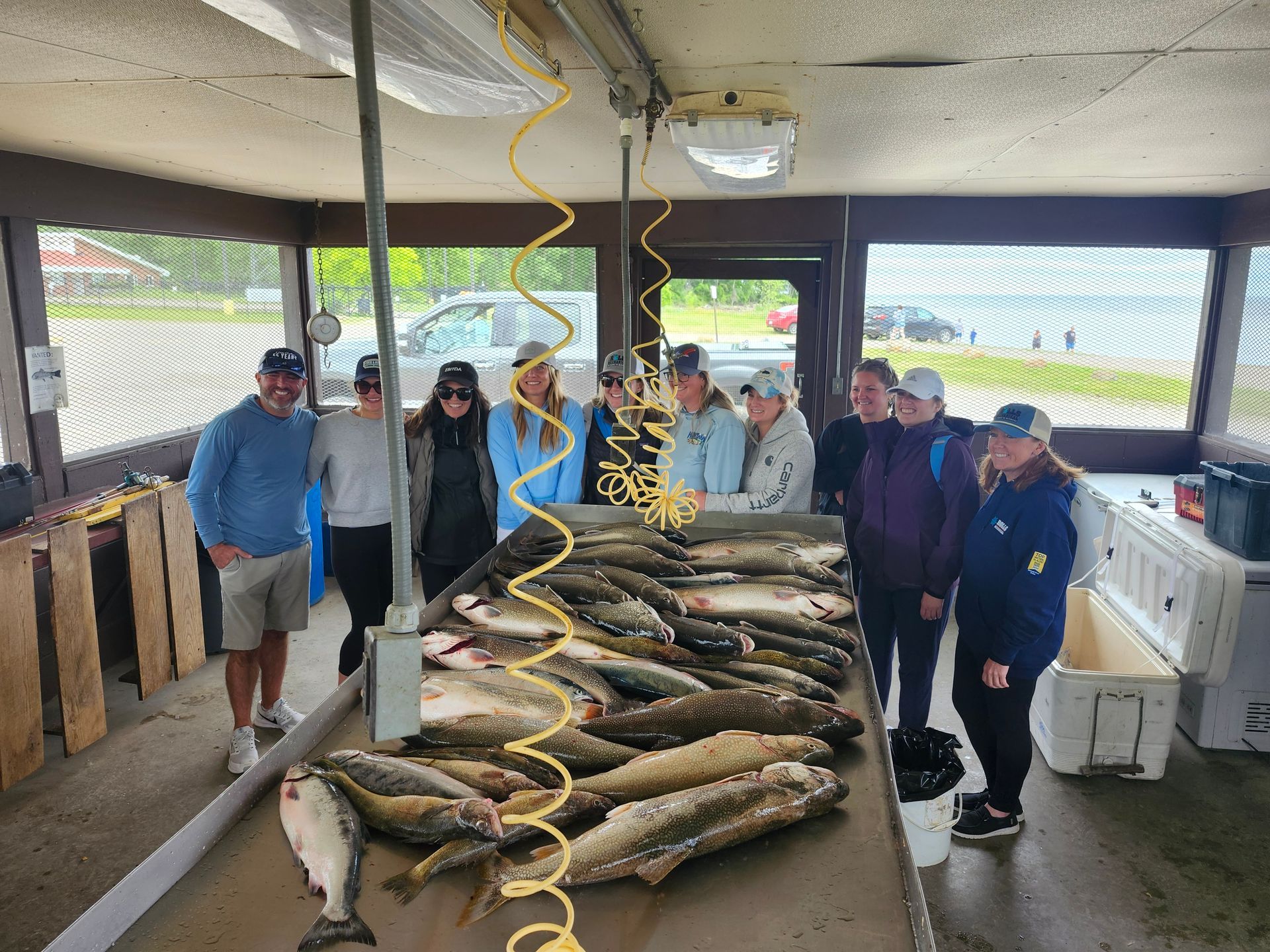 A group of people standing near a table filled with fish, inside a fish cleaning station near the water.