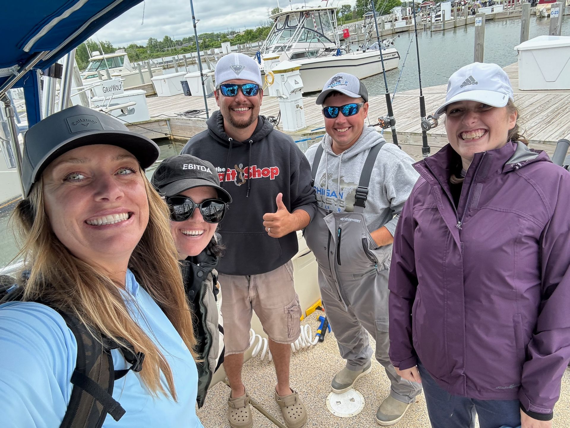 Five people smiling on a boat near a dock; one person gives a thumbs-up.