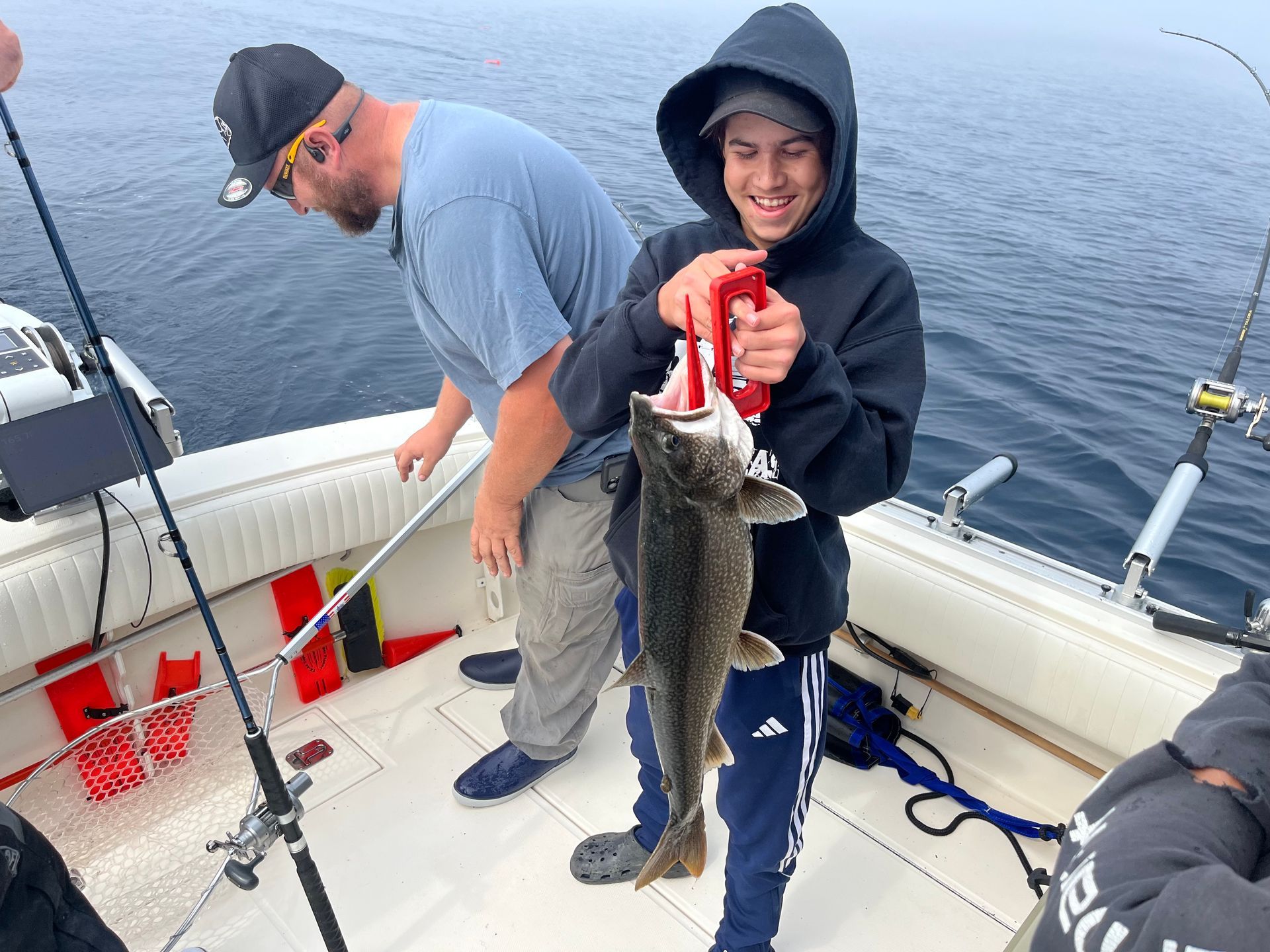 Boy smiling, holding fish on boat with man, sea in background.