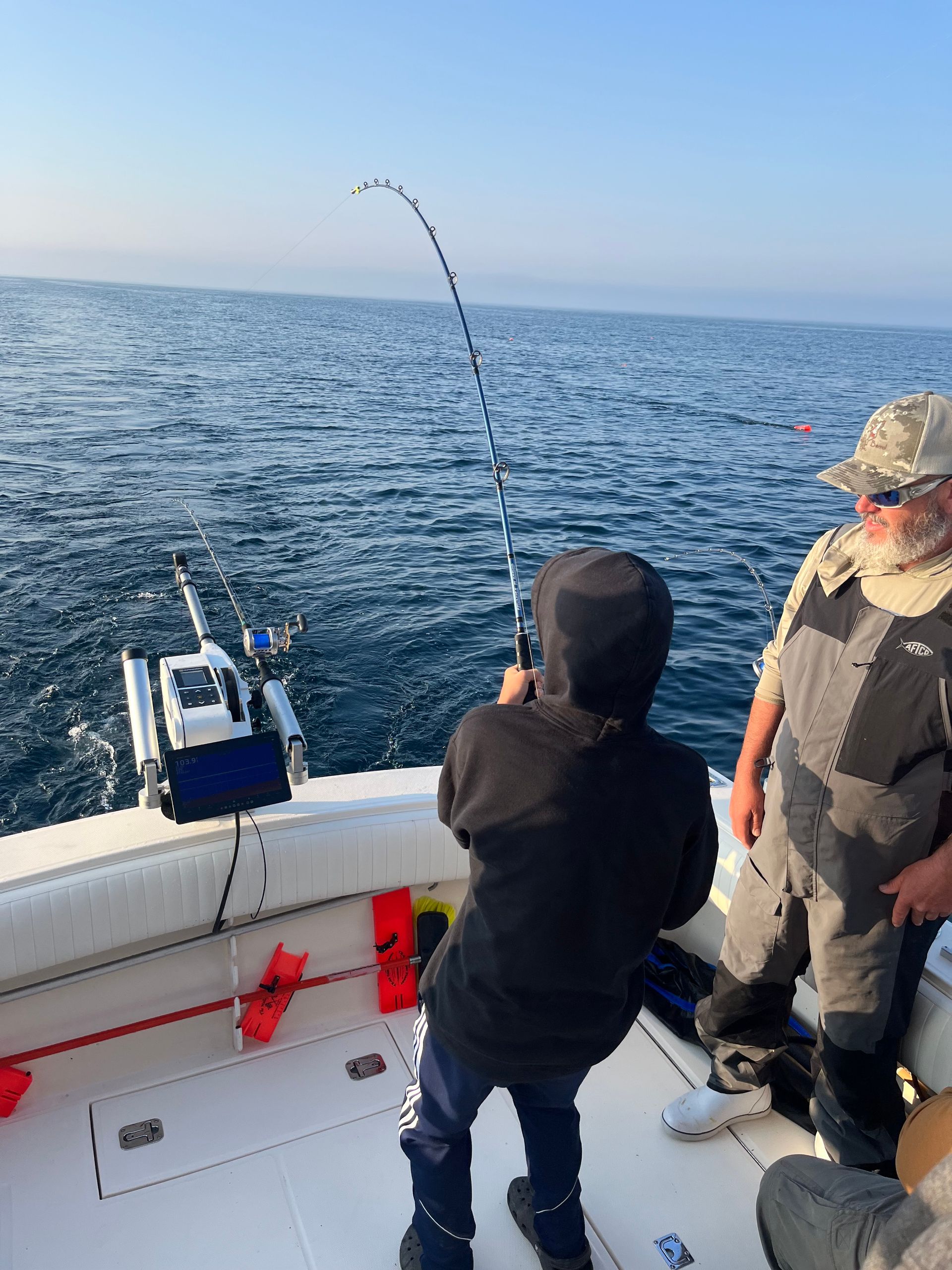 Boy fishing on a boat, rod bent, water and older man present.