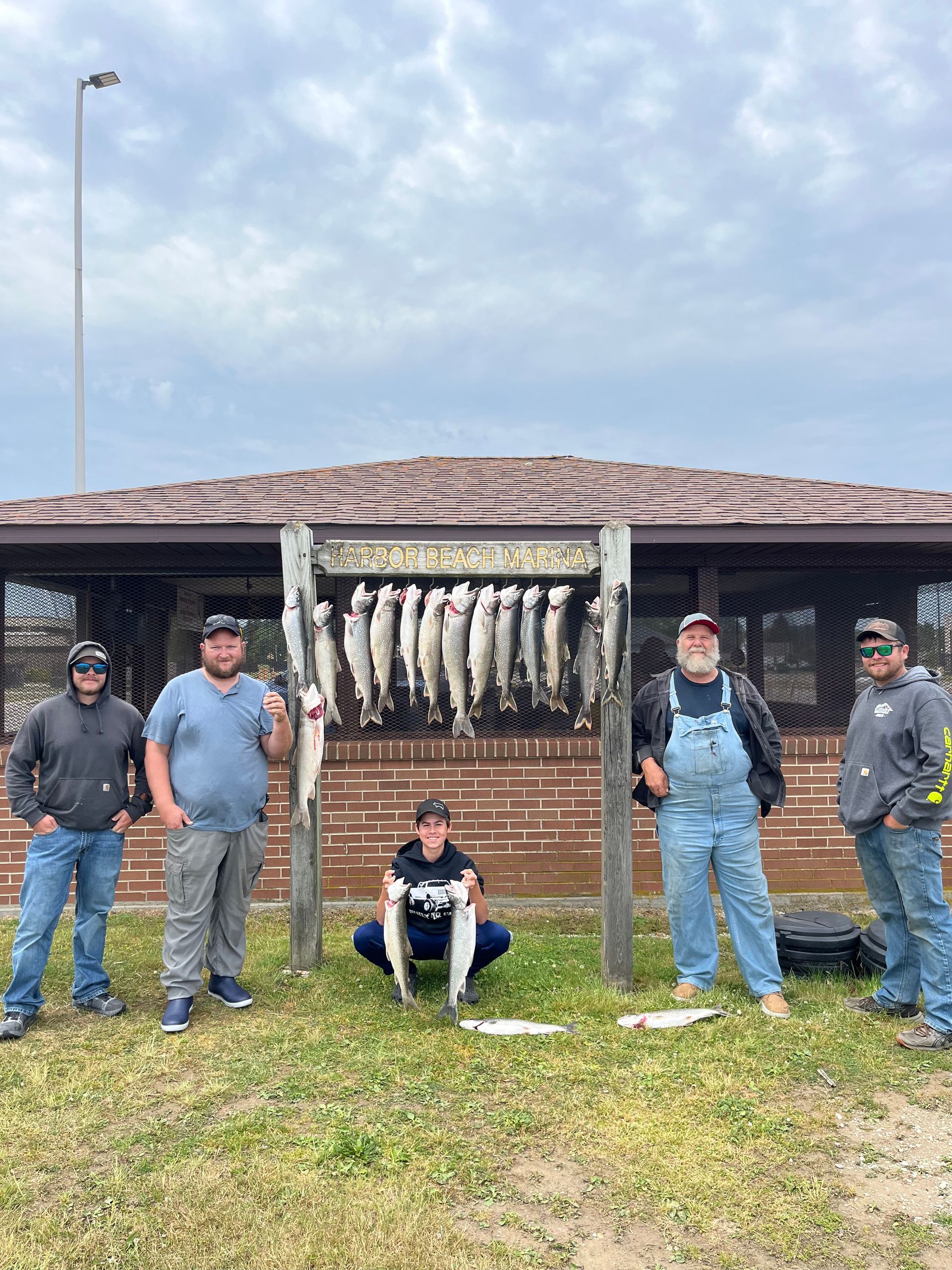 Group of five people with their fish catch, displayed on a wooden rack in front of a building.