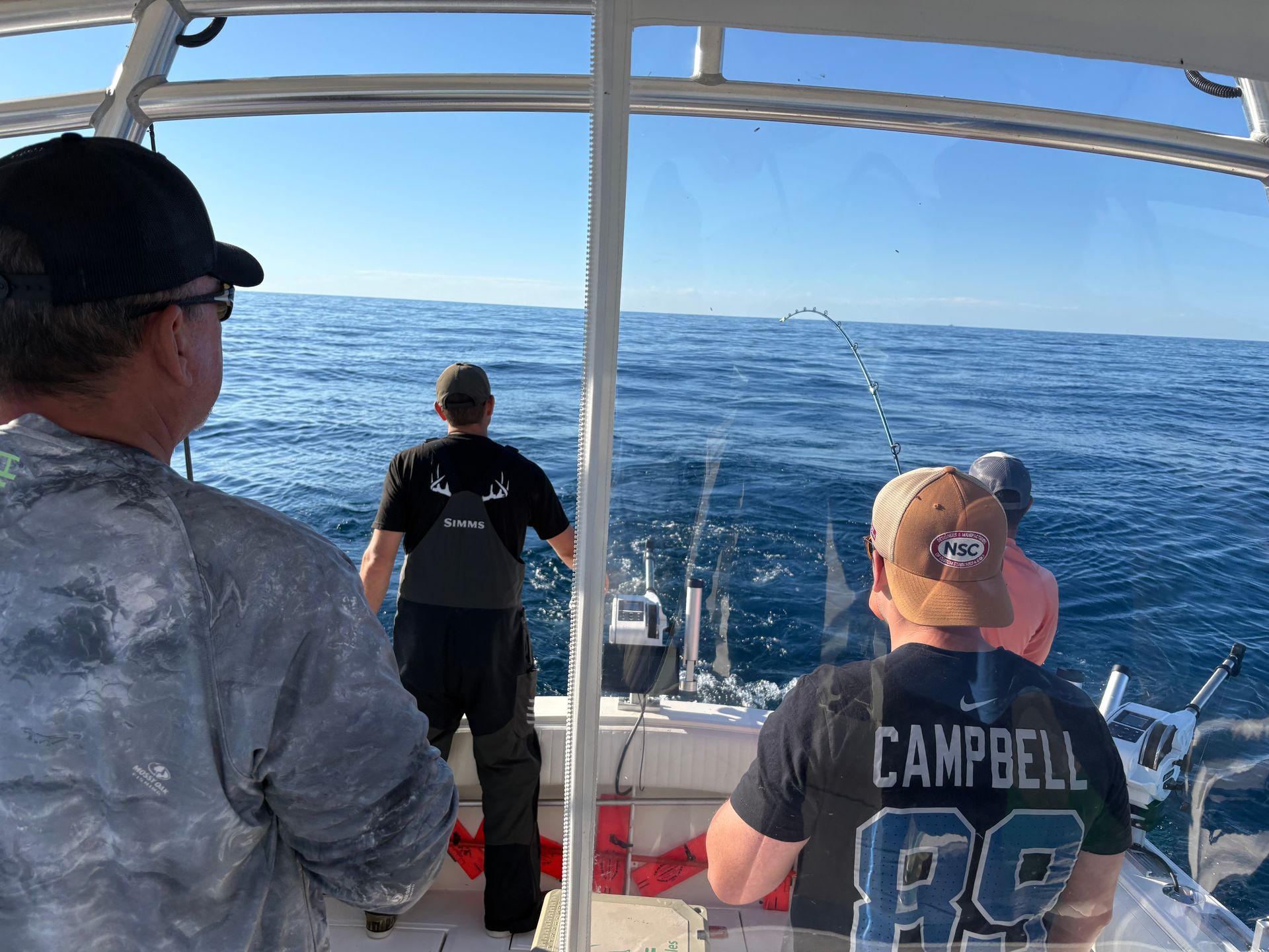 People fishing on a boat on a sunny day. One person is reeling in a fishing line.