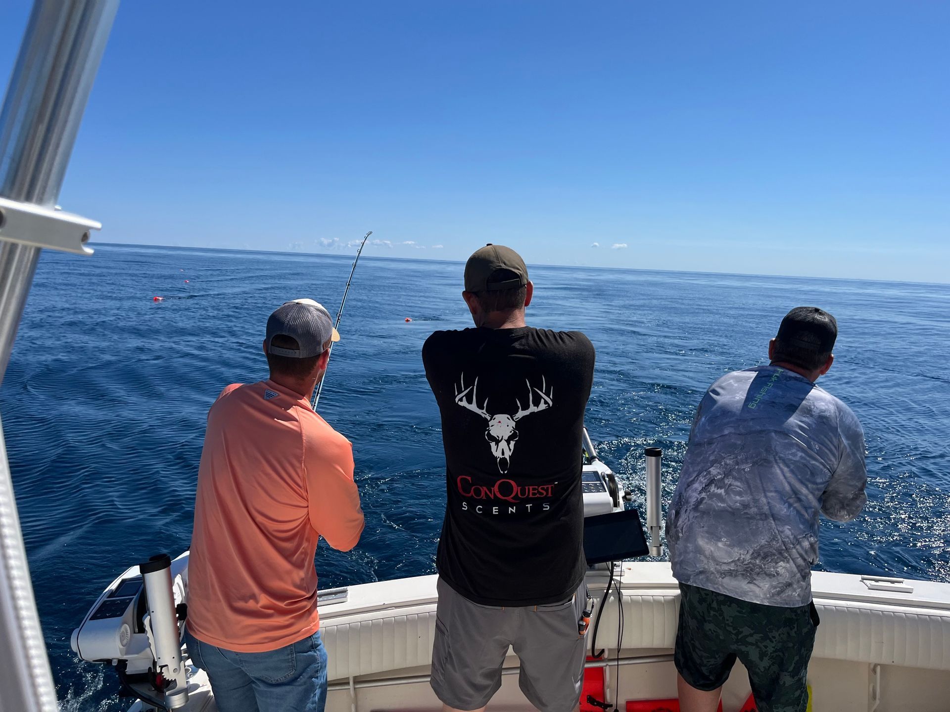 Three men fishing on a boat in the ocean on a sunny day.