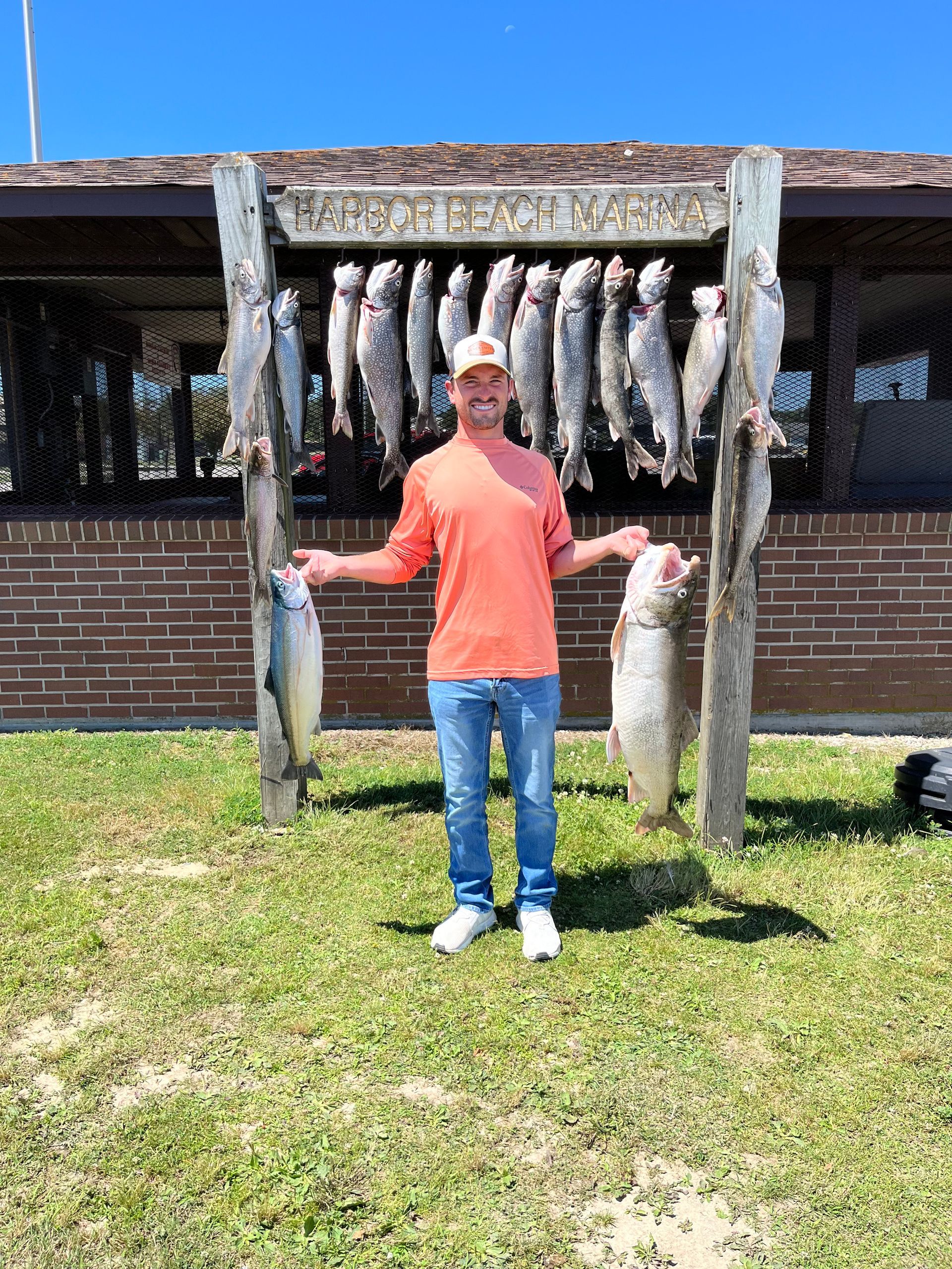 Man holding fish with a display of hanging fish. Outdoors, sunny day.