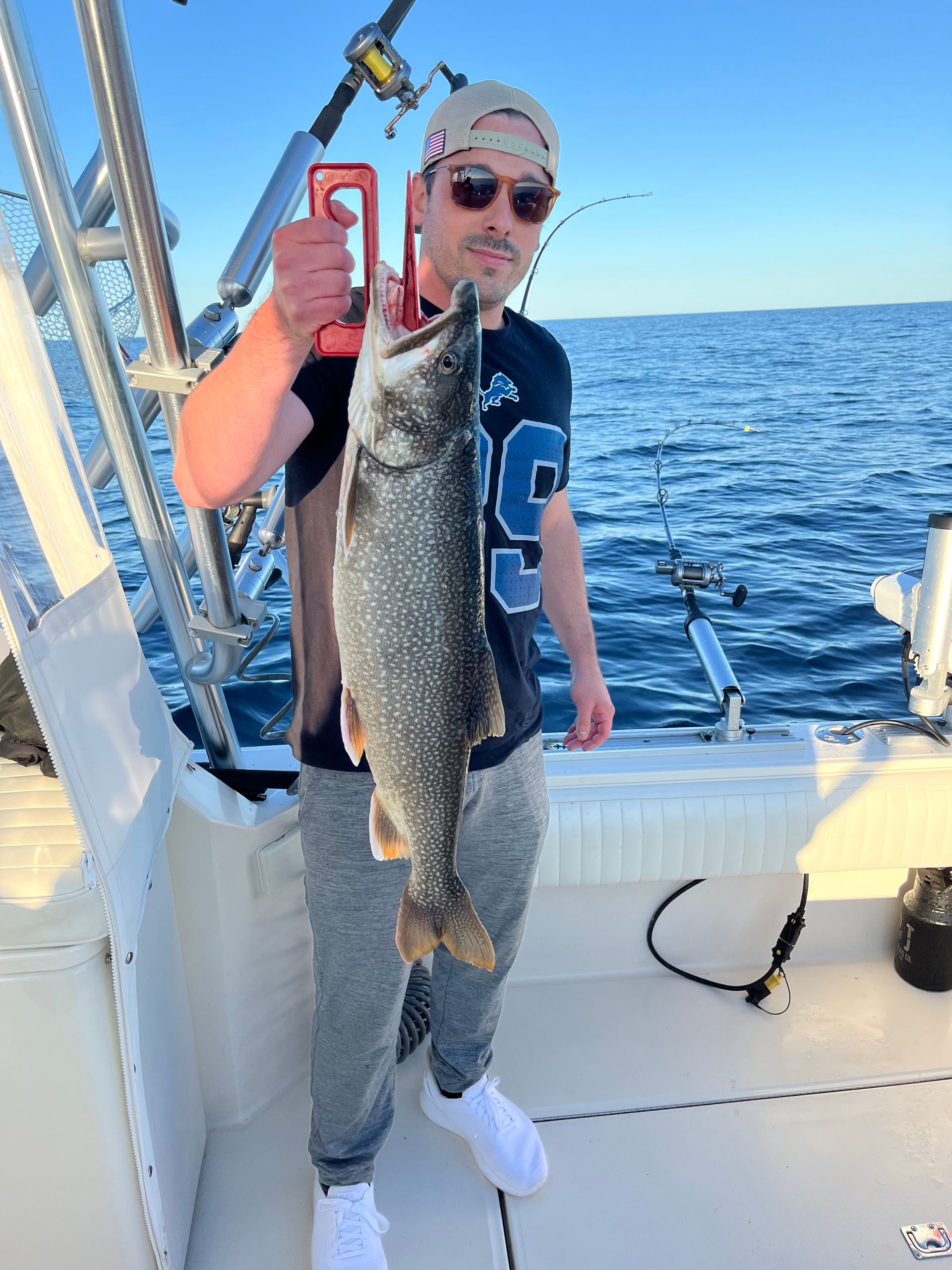 Man on boat holding a large fish, blue water in background.