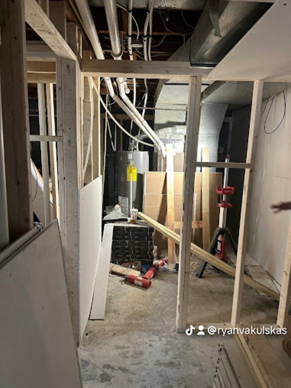 Basement under construction, wood framing, drywall, exposed pipes, concrete floor.