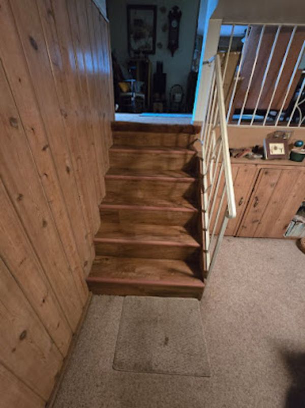 Wooden staircase leading up, with wood paneling on the walls and carpeted floor.