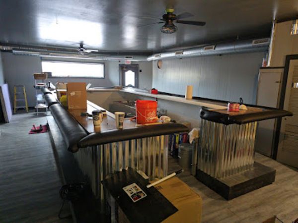 Interior of a bar under construction: long bar, metal detailing, paint buckets, unfinished ceiling.