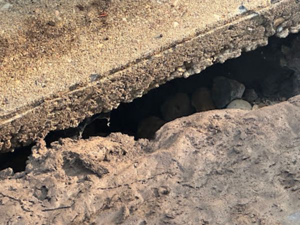 Hole in concrete with rocks visible, water droplets on the side. Dark interior.