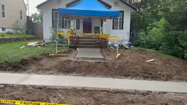 House under construction with new concrete walkway and porch. Yellow caution tape borders dirt and sidewalk.