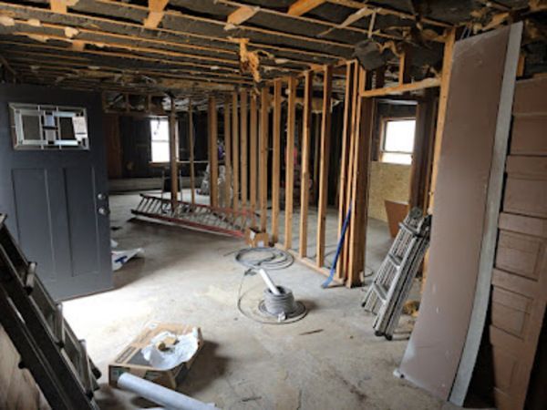 Interior of a room under renovation; exposed studs, debris on floor, unfinished walls, and an open door.