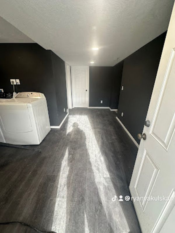 Laundry room with dark gray walls, white washer, and gray wood-look flooring.