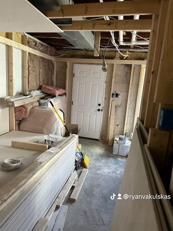 Basement under construction, studs, door, insulation, drywall, tools, and concrete floor.