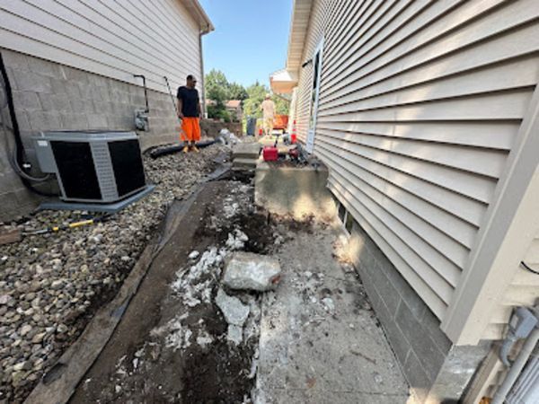 Construction zone between two houses; man in orange pants, gravel, dirt, concrete.