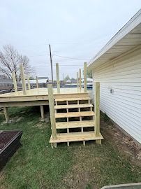 Wooden deck and stairs attached to a house on a grassy lawn, cloudy sky.