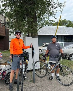 Two men are standing next to a bicycle and a refrigerator.