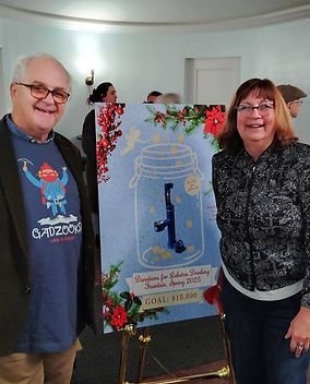 A man and a woman are standing next to a poster of a mason jar with a pipe in it.