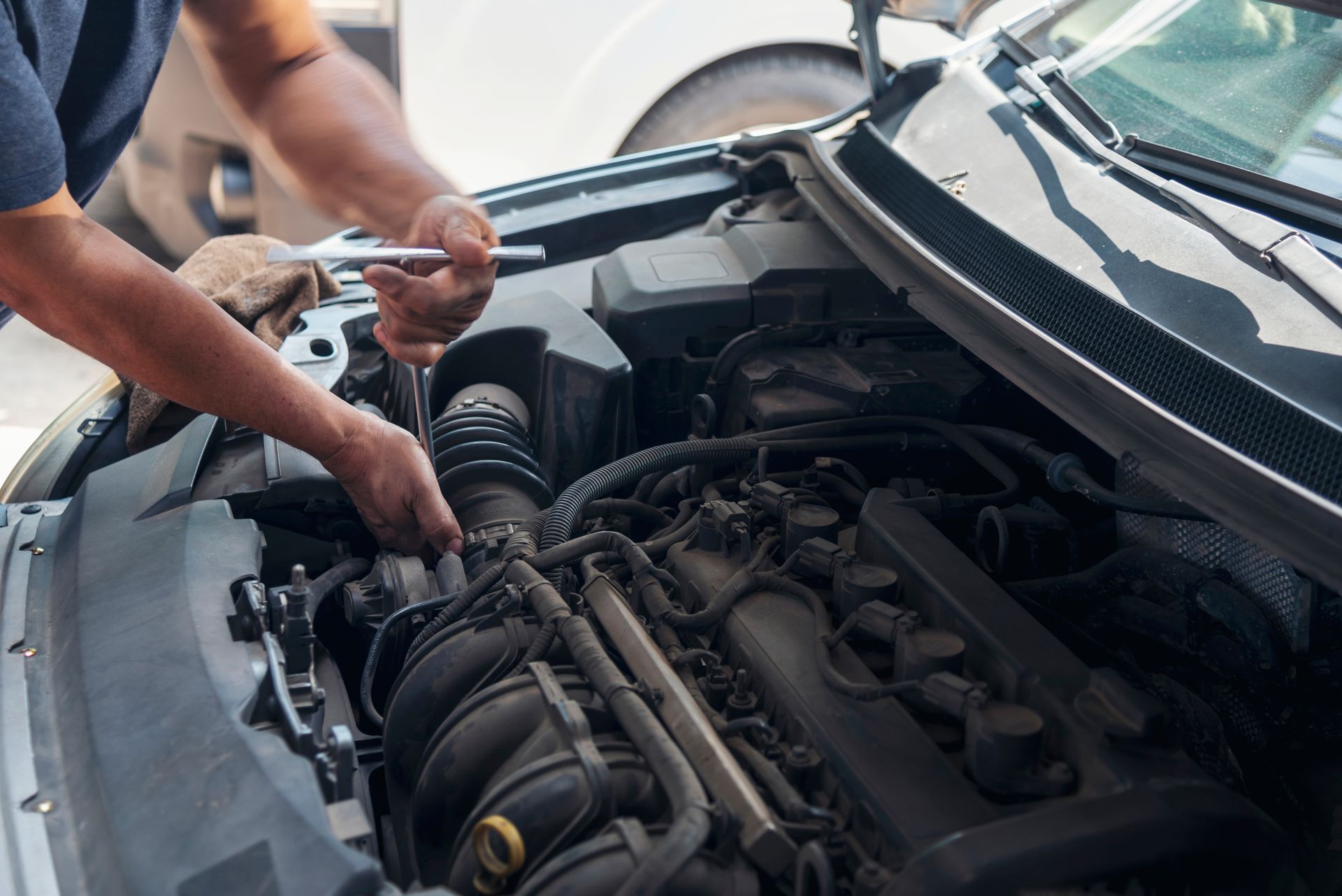A man is working on the engine of a car with a wrench.