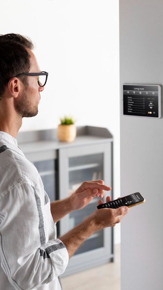 A man is using a smart phone and a remote control to control a smart home.