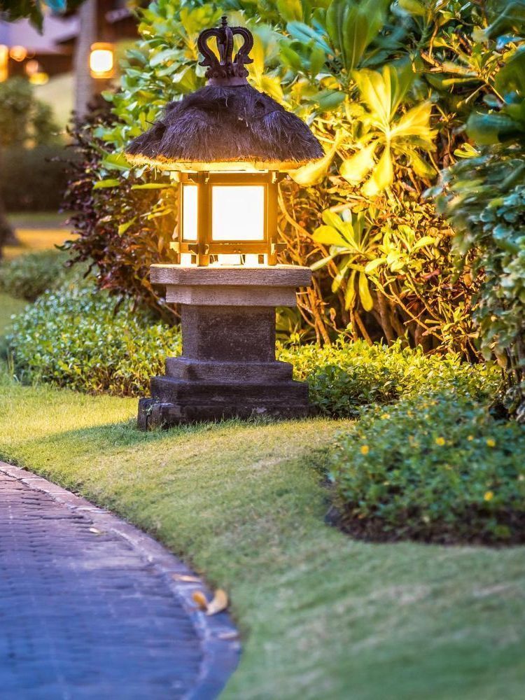 A lantern is lit up in the middle of a garden next to a path.