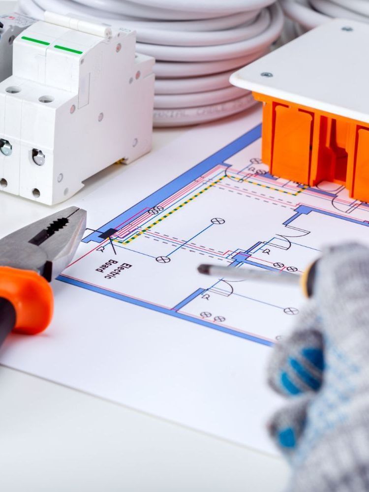 An electrician is working on a blueprint with a pair of pliers and a screwdriver.