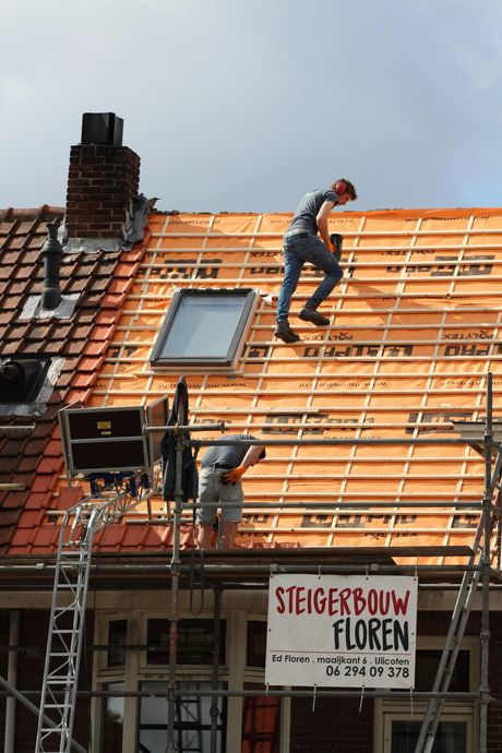 Two roofers working on a house roof with scaffolding, visible skylight, and sign.