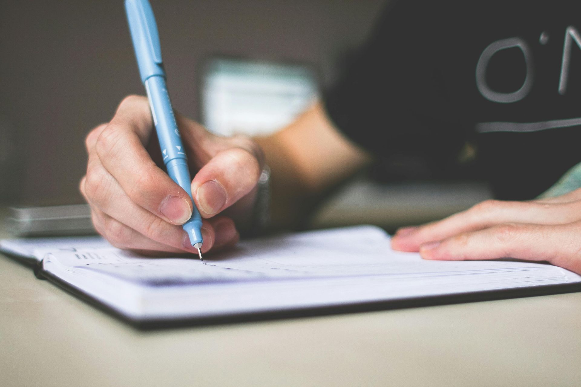 A man  writing in a notebook with a pen.