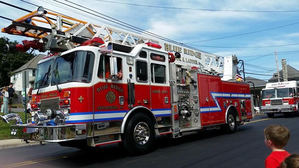 A red and white fire truck with a ladder is driving down a street.