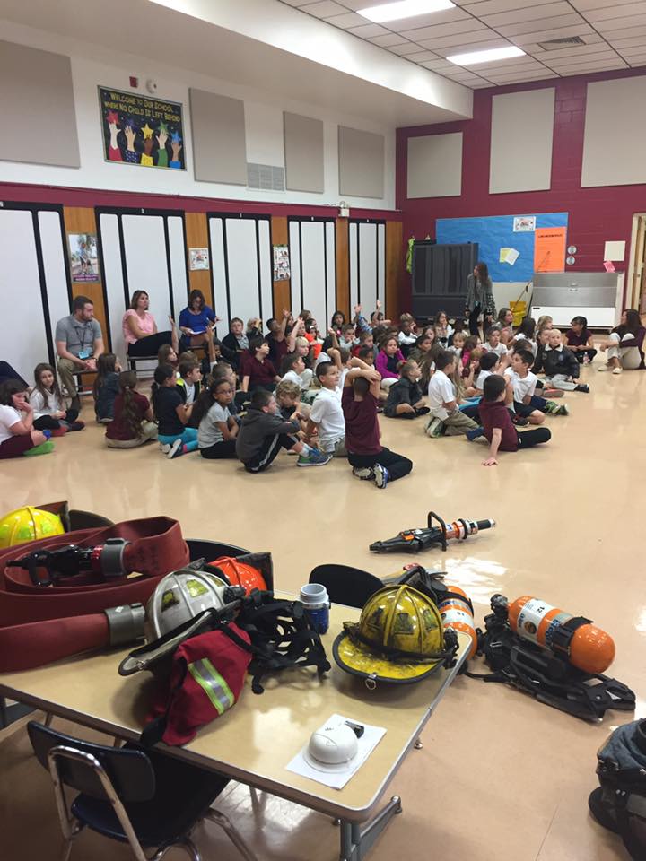 A group of children are sitting on the floor in a large room.