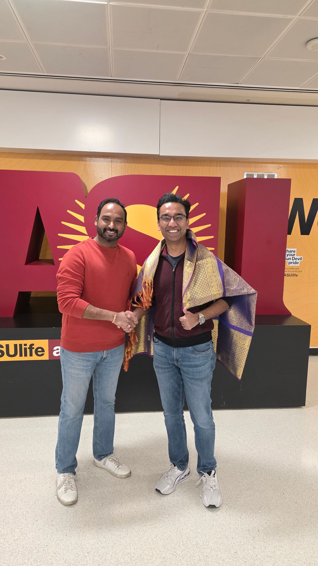 Two people posing indoors in front of a colorful display, smiling and standing close together.
