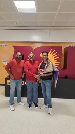 Three people standing together indoors in front of a stage, smiling and posing for a photo.