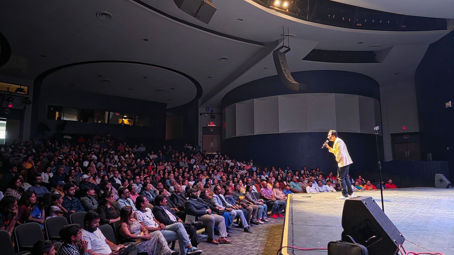 Speaker on stage addressing a packed auditorium audience in a large theater
