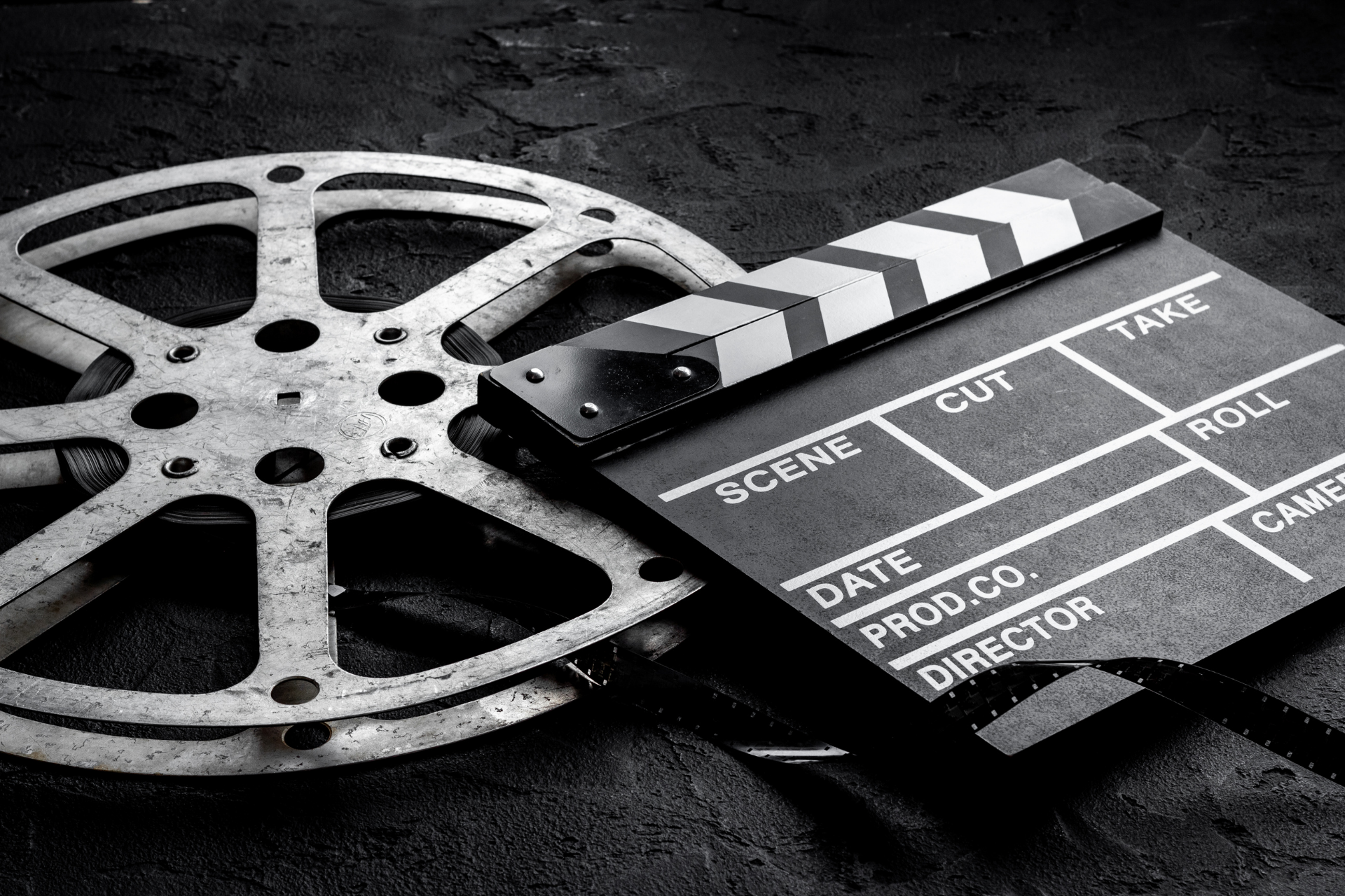 Film reel and clapperboard on a dark surface, suggesting movie production